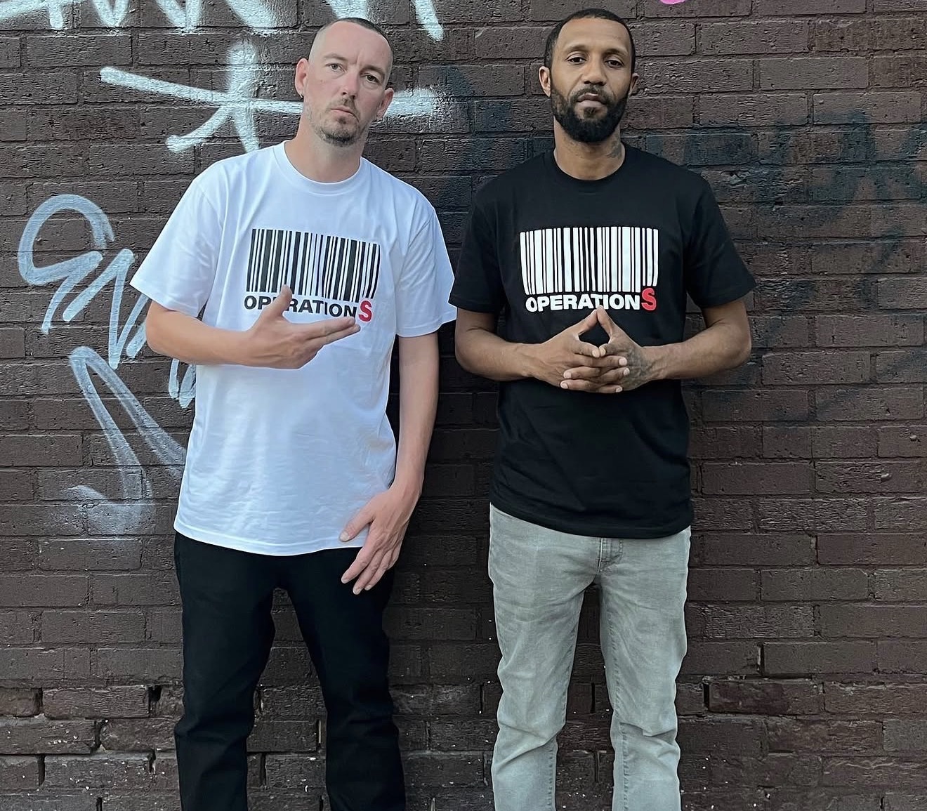 DJ Pure and MC Joe Fire against a graffiti brick wall